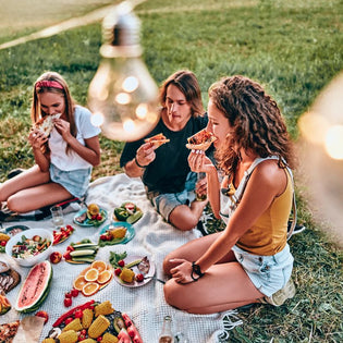  Summer picnic with friends enjoying fresh fruit, vegetables, and pizza on a blanket in the park
