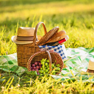  Summer picnic setup with wicker baskets, fresh grapes, baguette, wine bottle, and straw hats on green checkered blanket
