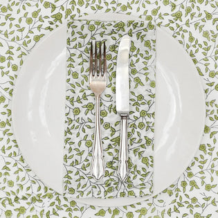  green floral napkin with a set of cutlery ontop under a plate and ontop of a floral table cloth